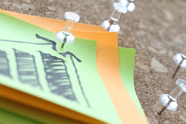 close up of pin and hand drawn business strategy graph chart on sticky note with cork board as concept